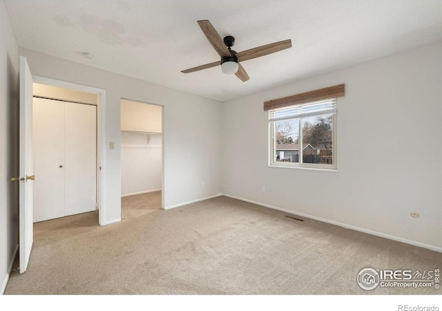 unfurnished bedroom featuring light carpet, a closet, ceiling fan, and a walk in closet