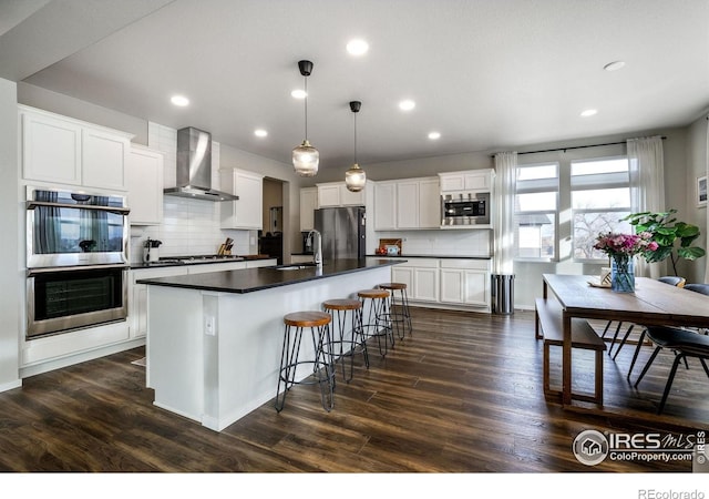 kitchen with white cabinets, decorative light fixtures, stainless steel appliances, and wall chimney range hood