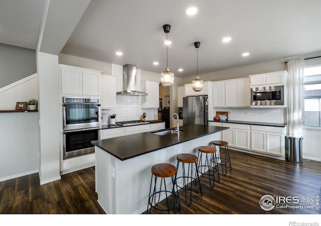 kitchen featuring appliances with stainless steel finishes, dark hardwood / wood-style flooring, wall chimney exhaust hood, sink, and decorative light fixtures