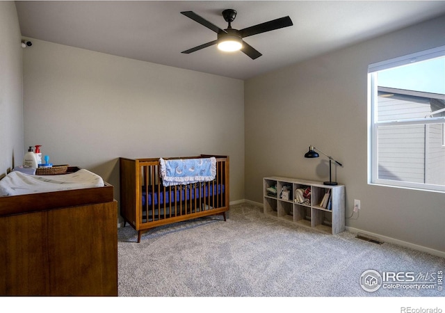 bedroom featuring ceiling fan, a crib, and light carpet