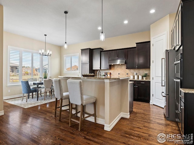 kitchen featuring dark hardwood / wood-style flooring, tasteful backsplash, decorative light fixtures, an inviting chandelier, and an island with sink