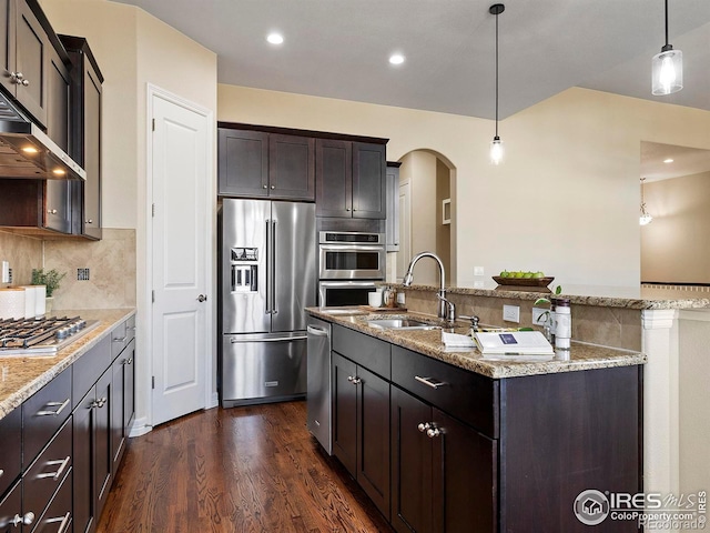 kitchen with sink, stainless steel appliances, dark hardwood / wood-style floors, decorative light fixtures, and a center island with sink