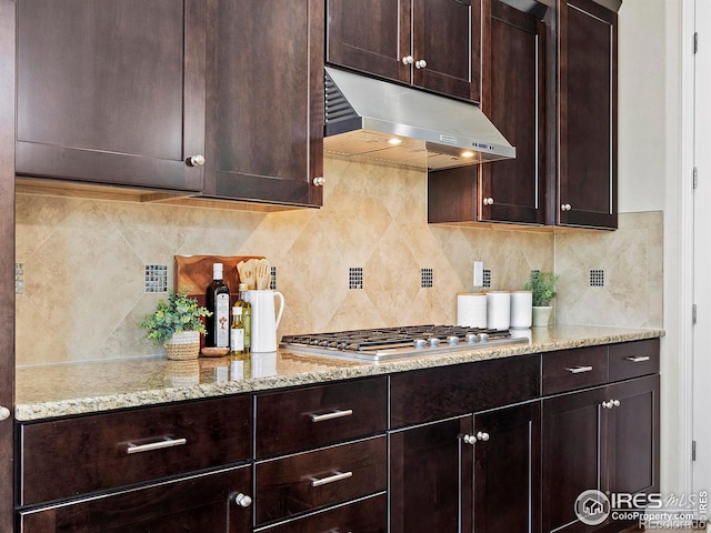 kitchen with stainless steel gas stovetop, dark brown cabinets, light stone countertops, and backsplash