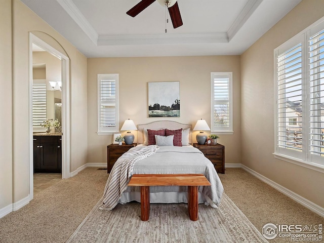 carpeted bedroom with ceiling fan, a raised ceiling, ornamental molding, and ensuite bathroom