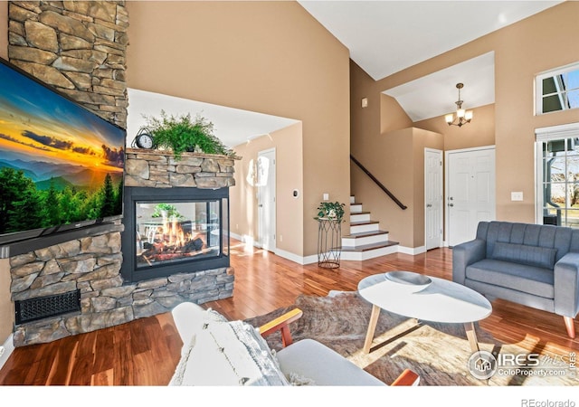 living room featuring hardwood / wood-style floors, high vaulted ceiling, a stone fireplace, and a notable chandelier