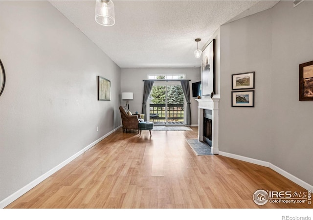 living area with a tiled fireplace, light hardwood / wood-style flooring, and a textured ceiling