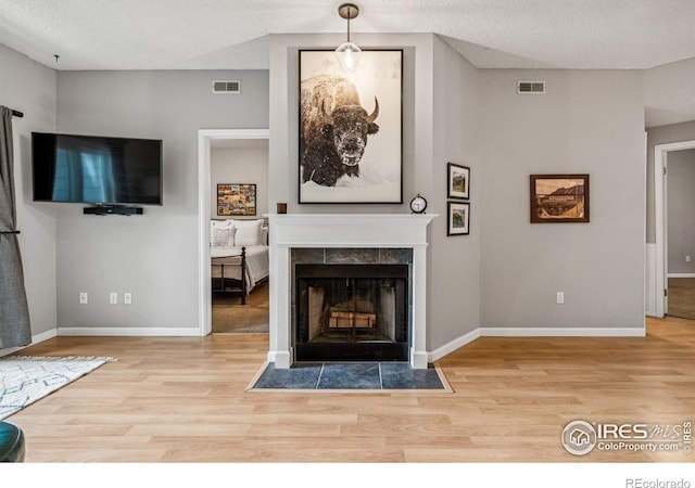 unfurnished living room with light wood-type flooring, a textured ceiling, and a tiled fireplace