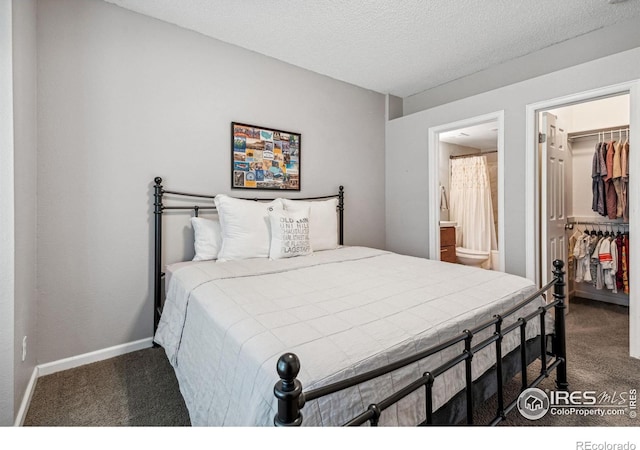 bedroom with ensuite bath, a textured ceiling, a walk in closet, a closet, and dark carpet