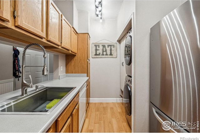 kitchen featuring light wood-type flooring, white dishwasher, stacked washer / dryer, and sink