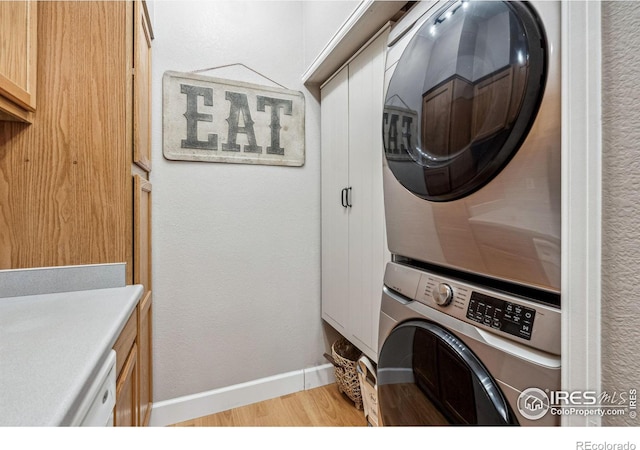 laundry room with stacked washer / drying machine, light hardwood / wood-style floors, and cabinets