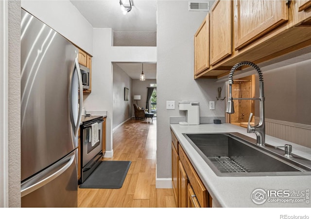 kitchen featuring sink, light hardwood / wood-style flooring, hanging light fixtures, and appliances with stainless steel finishes