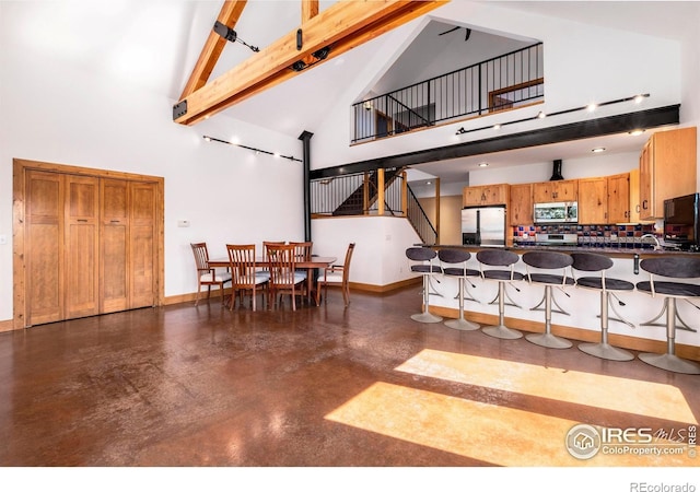 kitchen featuring beam ceiling, stainless steel appliances, high vaulted ceiling, a breakfast bar area, and decorative backsplash