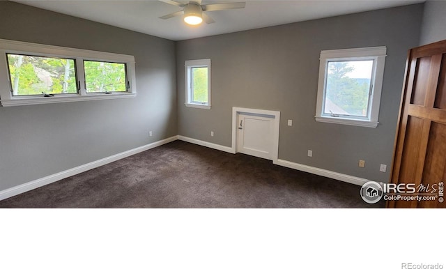 spare room with dark colored carpet, plenty of natural light, and ceiling fan