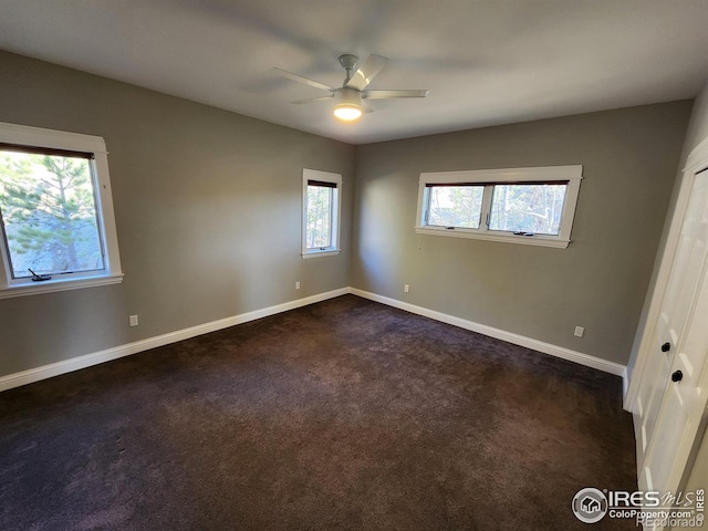 unfurnished bedroom featuring multiple windows, ceiling fan, and dark colored carpet