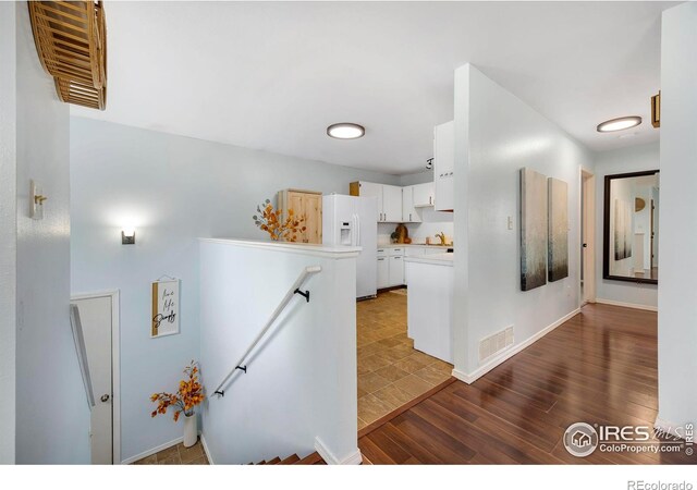 kitchen featuring white cabinetry, white fridge with ice dispenser, and dark wood-type flooring