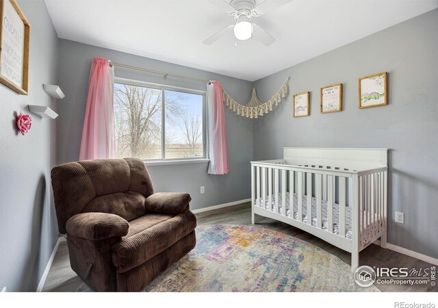 bedroom with hardwood / wood-style flooring, ceiling fan, and a nursery area