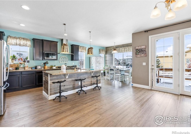 kitchen featuring a healthy amount of sunlight, a kitchen island, hanging light fixtures, and wall chimney range hood