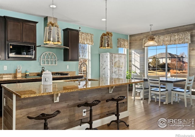 kitchen featuring pendant lighting, a breakfast bar area, light stone counters, dark brown cabinetry, and built in microwave