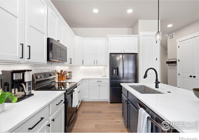 kitchen featuring stainless steel appliances, white cabinetry, hanging light fixtures, and light hardwood / wood-style floors