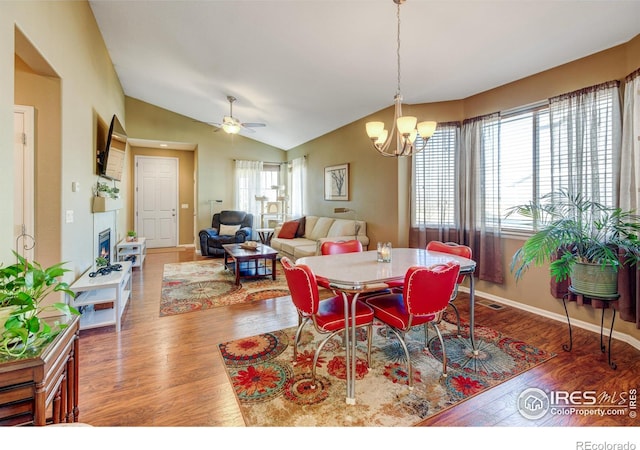 dining area with ceiling fan with notable chandelier, wood-type flooring, and lofted ceiling