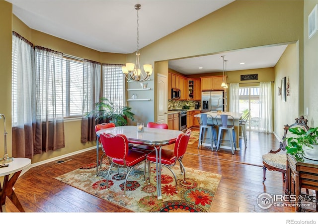 dining space with a notable chandelier, vaulted ceiling, and hardwood / wood-style flooring