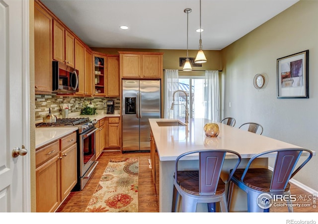 kitchen with sink, hanging light fixtures, stainless steel appliances, a kitchen island with sink, and light wood-type flooring