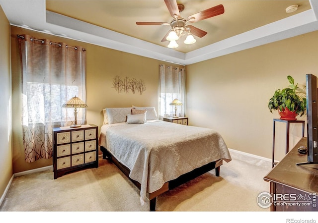 bedroom with light carpet, a raised ceiling, and ceiling fan