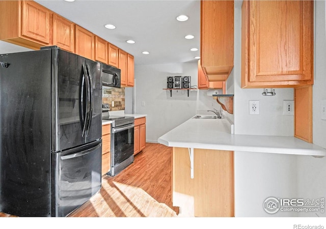 kitchen with black appliances, sink, light hardwood / wood-style floors, a kitchen bar, and kitchen peninsula