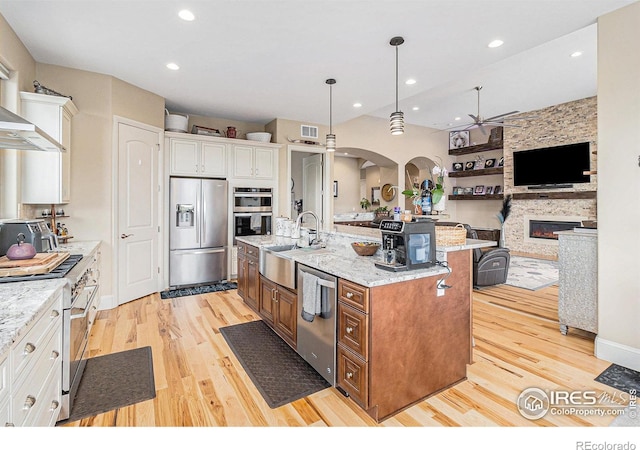 kitchen featuring white cabinetry, sink, hanging light fixtures, stainless steel appliances, and a kitchen island with sink