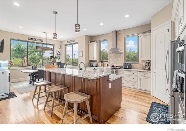 kitchen with pendant lighting, wall chimney exhaust hood, plenty of natural light, and an island with sink