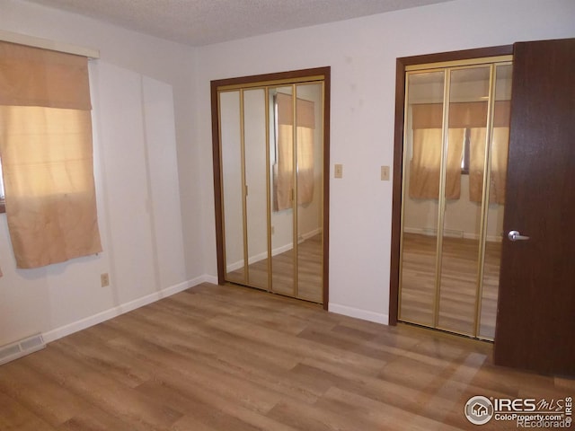 unfurnished bedroom with two closets, a textured ceiling, and light hardwood / wood-style flooring