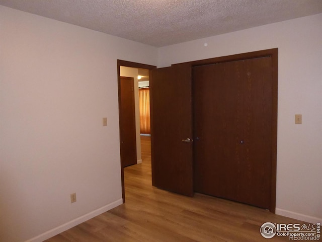 unfurnished bedroom with a textured ceiling, light wood-type flooring, and a closet