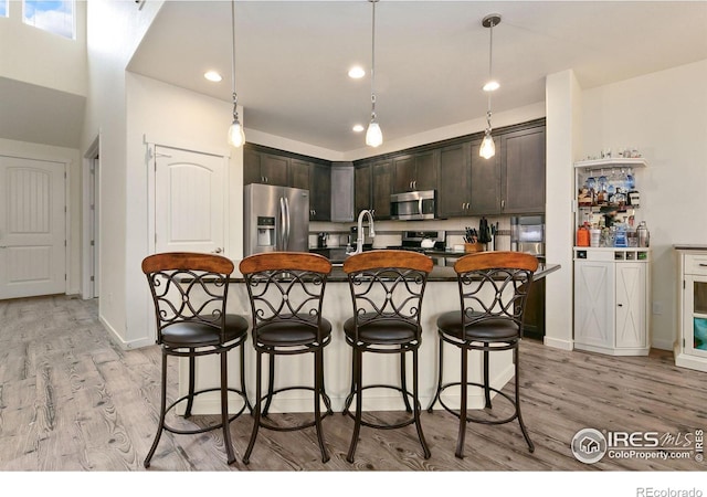 kitchen featuring light wood-style floors, stainless steel appliances, dark countertops, and a breakfast bar