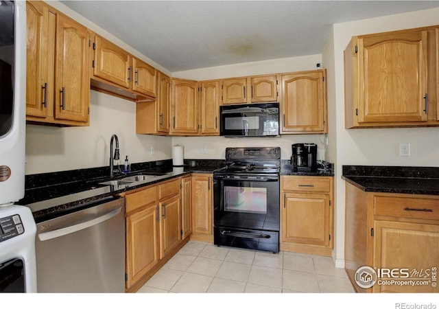 kitchen with sink, dark stone countertops, stacked washer / drying machine, light tile patterned floors, and black appliances