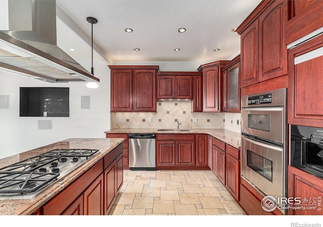 kitchen with sink, appliances with stainless steel finishes, light stone counters, island exhaust hood, and decorative light fixtures