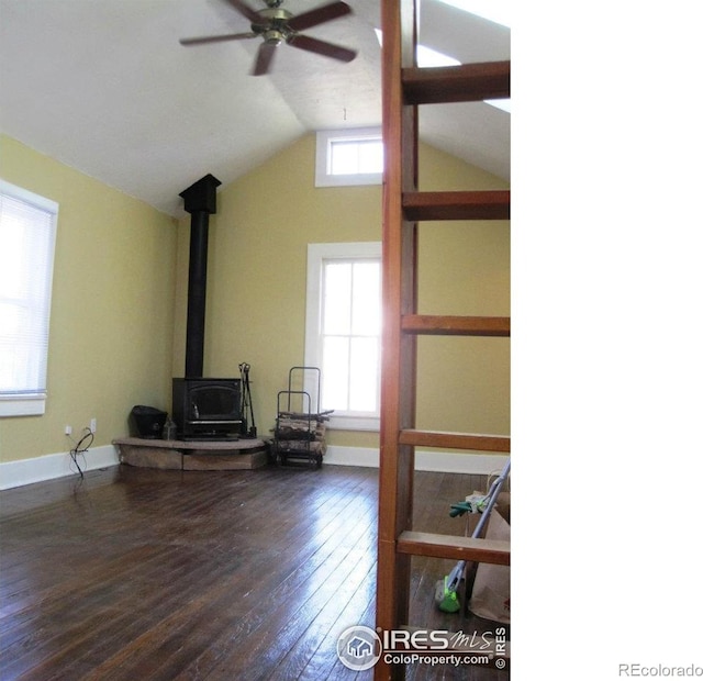 unfurnished living room featuring a wood stove, ceiling fan, dark wood-type flooring, and vaulted ceiling