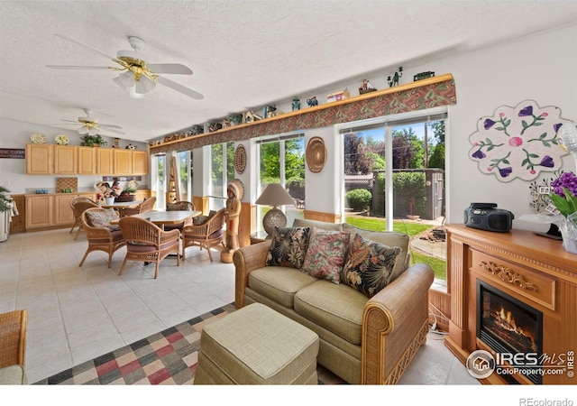 living area with a textured ceiling, light tile patterned floors, a glass covered fireplace, and a ceiling fan