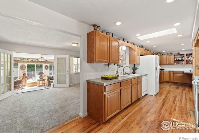 kitchen with light carpet, white appliances, a skylight, light wood-style flooring, and a sink