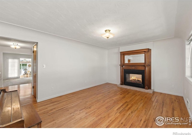 unfurnished living room with light wood-type flooring, baseboards, a textured ceiling, and a multi sided fireplace