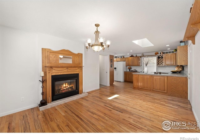 kitchen with a peninsula, white fridge with ice dispenser, light wood finished floors, a glass covered fireplace, and decorative light fixtures