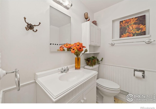 half bath with a wainscoted wall, toilet, and vanity