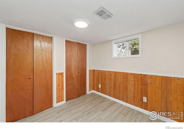 unfurnished bedroom featuring wooden walls, visible vents, wainscoting, wood finished floors, and a textured ceiling