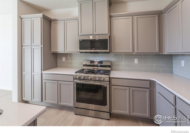 5086 Mckinnon Ct, Timnath, CO 80547 - kitchen with appliances with stainless steel finishes, gray cabinets, light countertops, light wood finished floors, and decorative backsplash