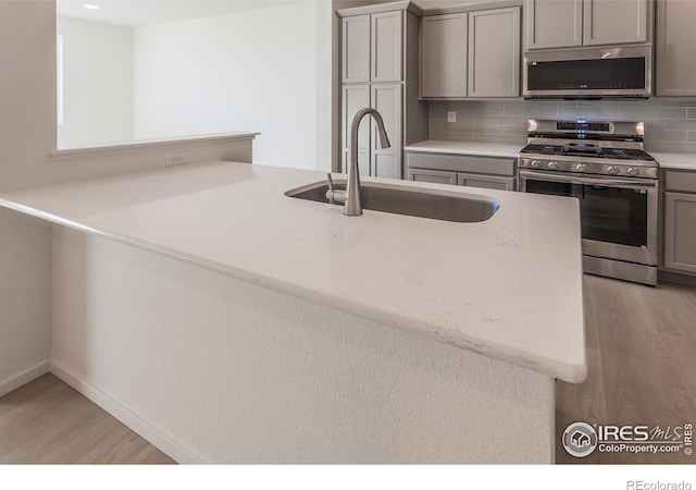 5086 Mckinnon Ct, Timnath, CO 80547 - kitchen with stainless steel appliances, gray cabinetry, light wood-style flooring, decorative backsplash, and light stone counters
