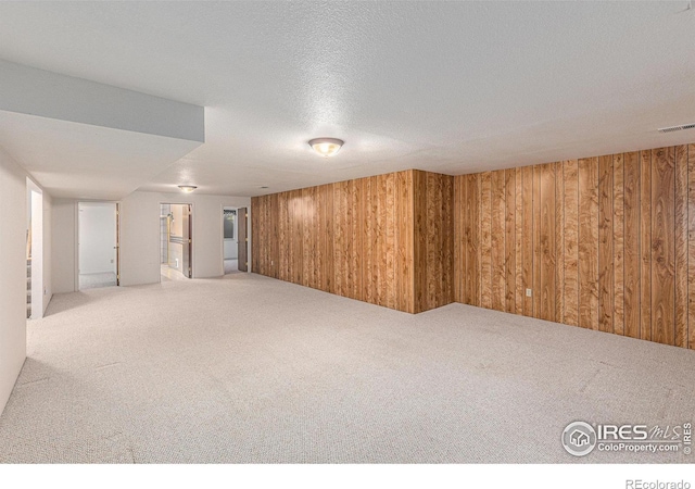 basement with carpet flooring, wood walls, and a textured ceiling