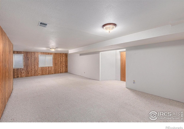 basement featuring wood walls, light colored carpet, and a textured ceiling