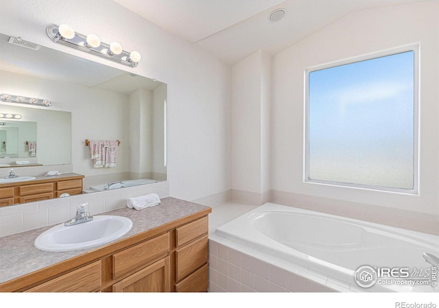 bathroom featuring a relaxing tiled tub, vanity, and vaulted ceiling