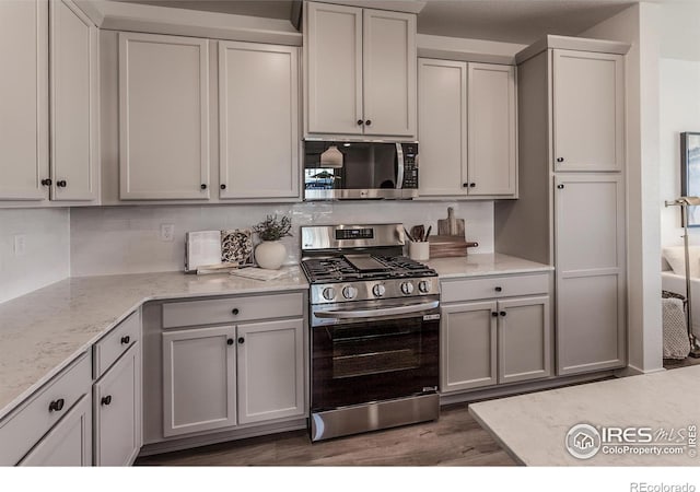 kitchen with stainless steel appliances, light stone countertops, backsplash, and wood finished floors