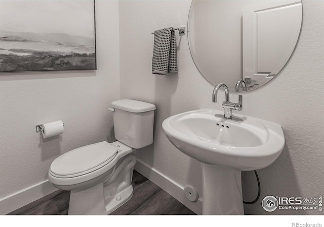 half bath with baseboards, toilet, and wood finished floors