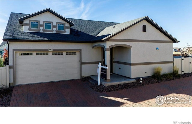 view of front of house featuring decorative driveway, fence, and stucco siding